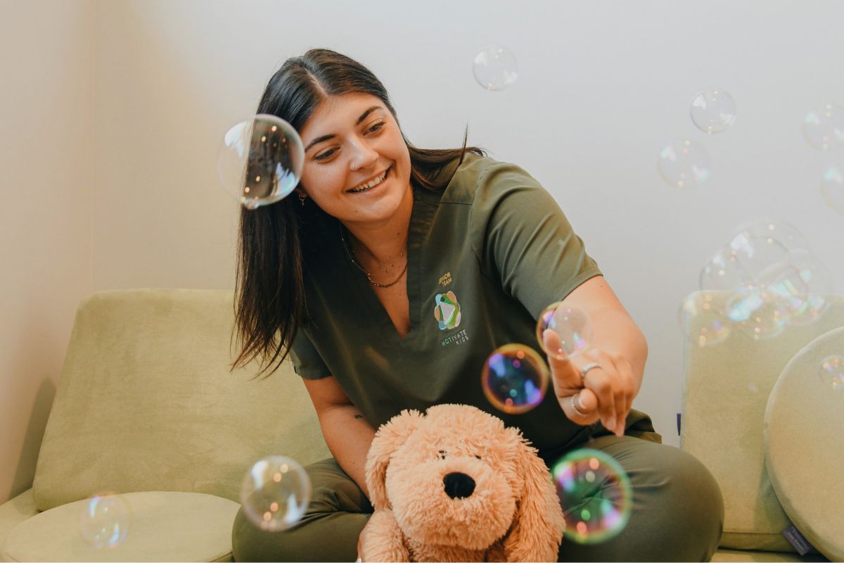 A woman sitting on a sofa with a soft toy and playfully popping bubbles in the air.