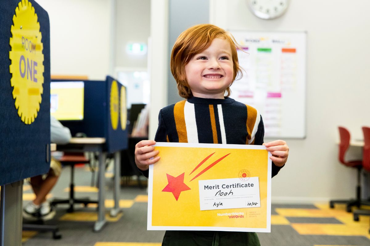A young boy proudly displays his certificate at Number Works n Words, Adelaide