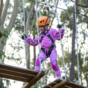 A girl in purple jumpsuit and orange helmet ziplining at Treeclimb Adelaide.