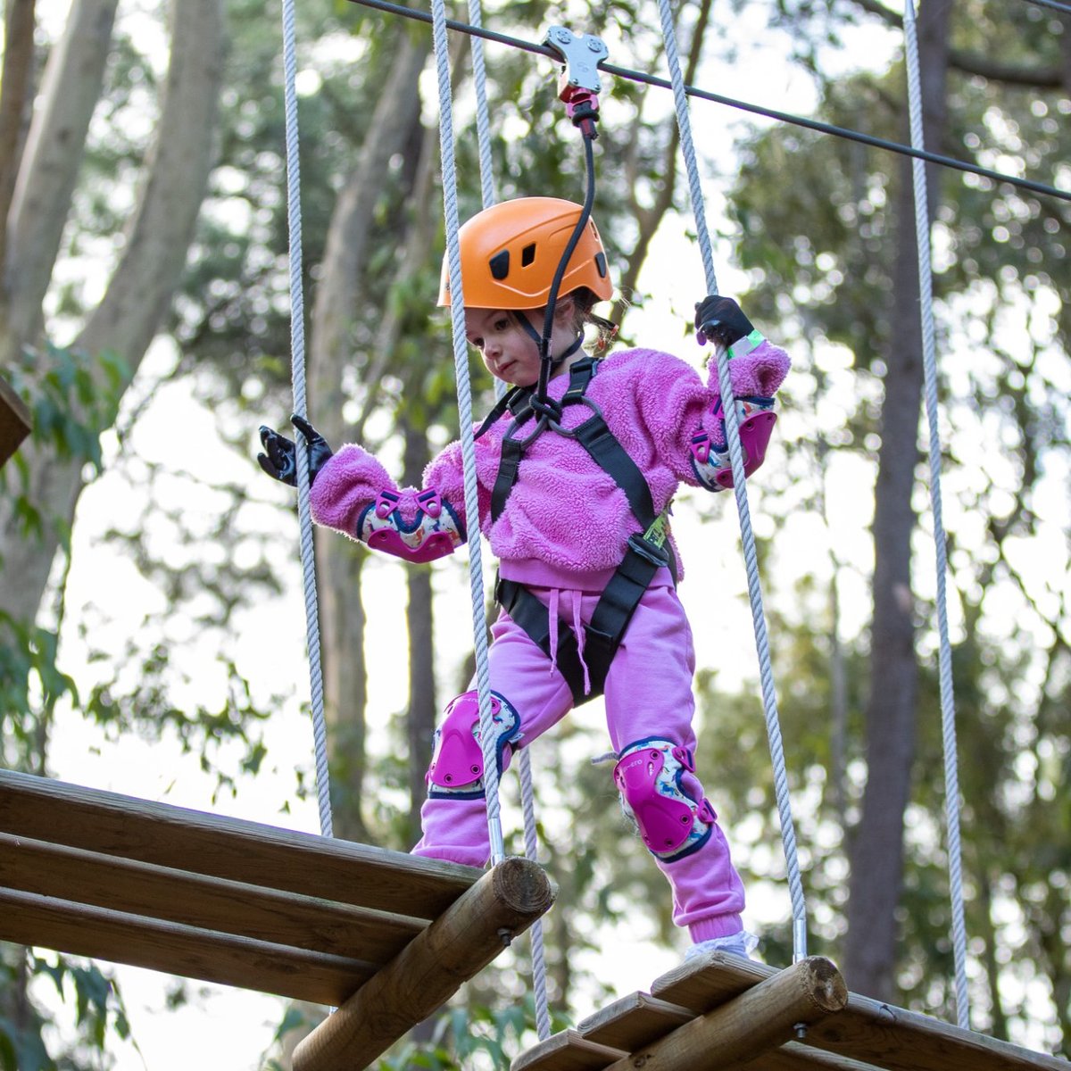 A girl in purple jumpsuit and orange helmet ziplining at Treeclimb Adelaide.