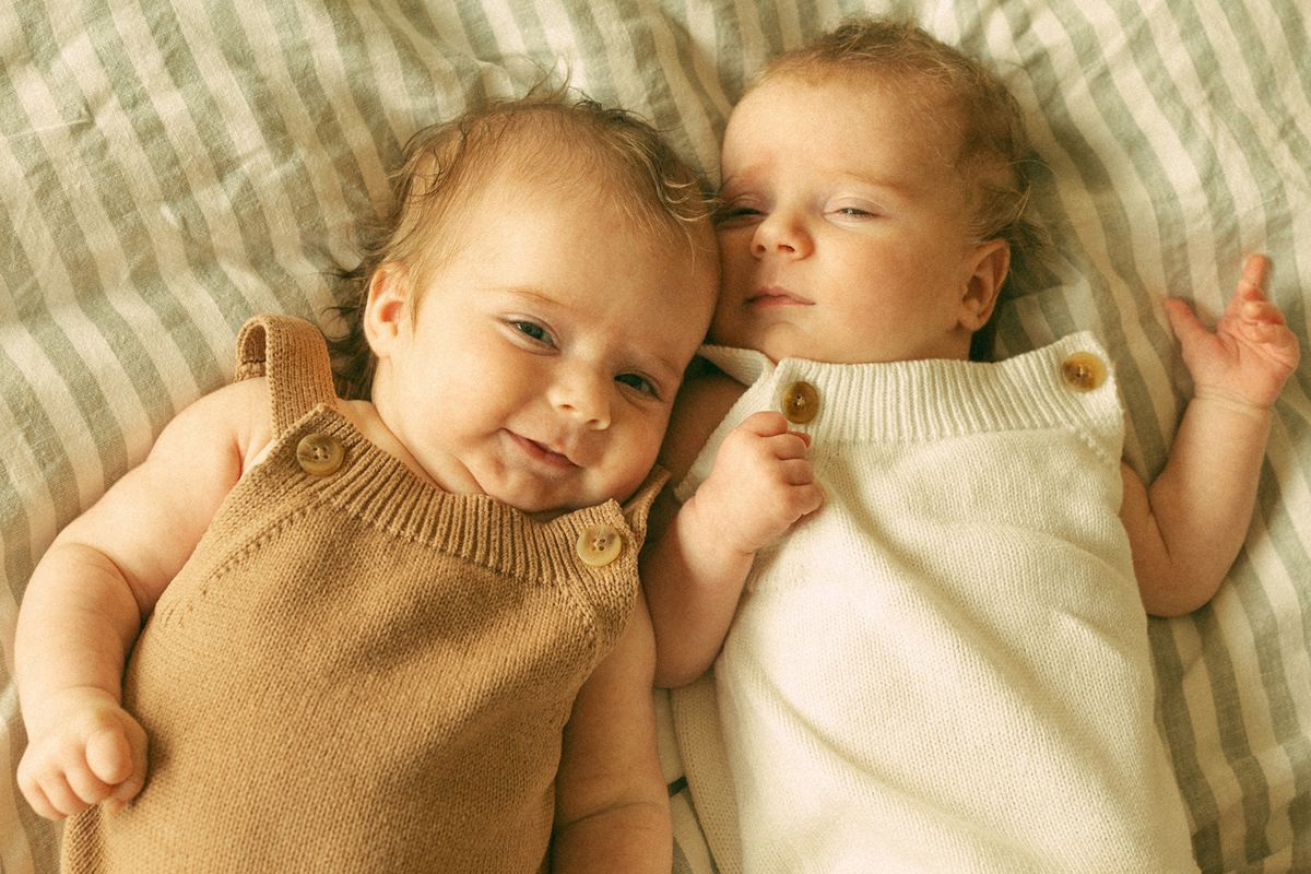 Twin babies lying side by side on a blanket