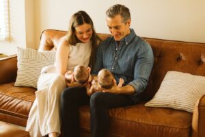 Parents sitting on a couch holding their twin babies
