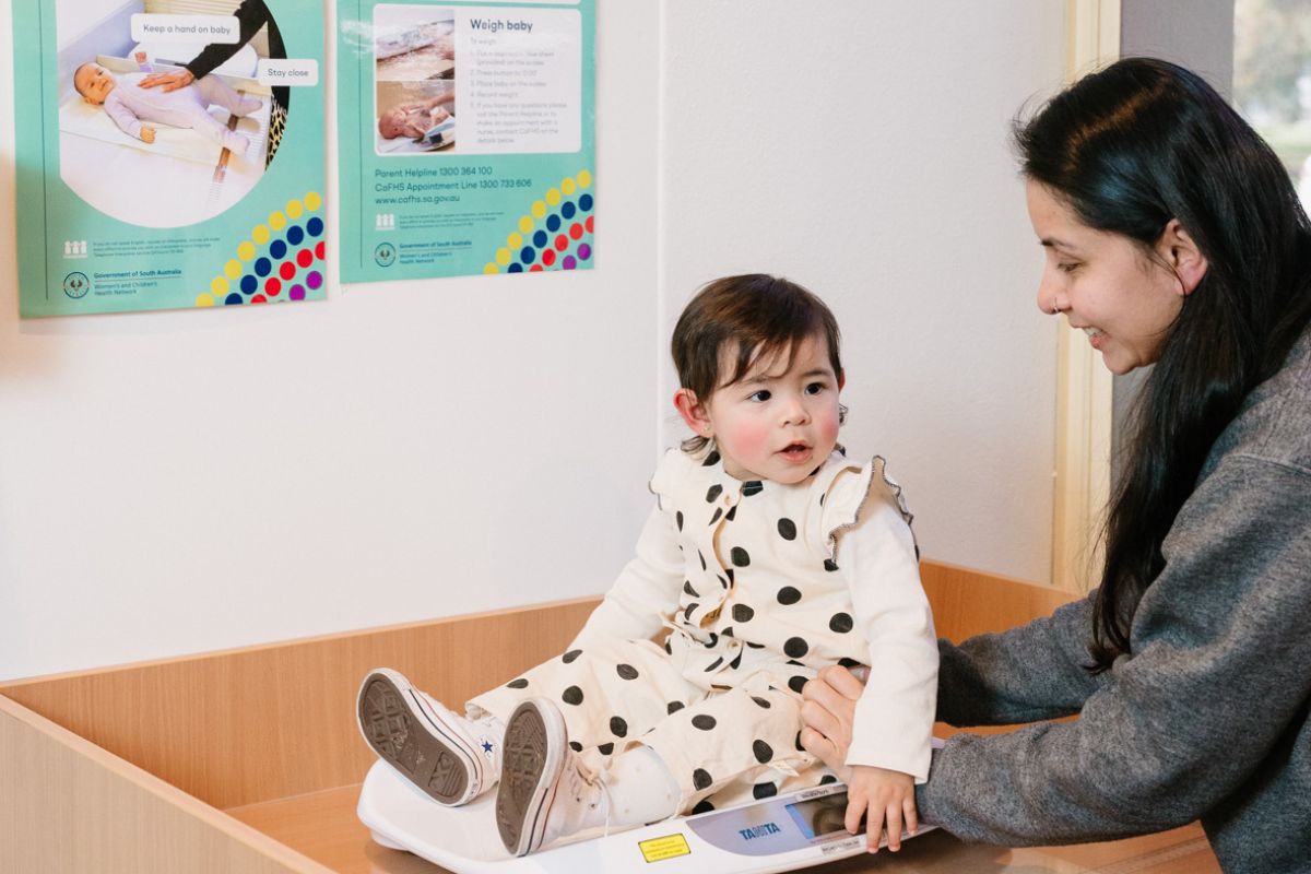 A baby in a CAFHS appointment sitting on a scale held up by a nurse.