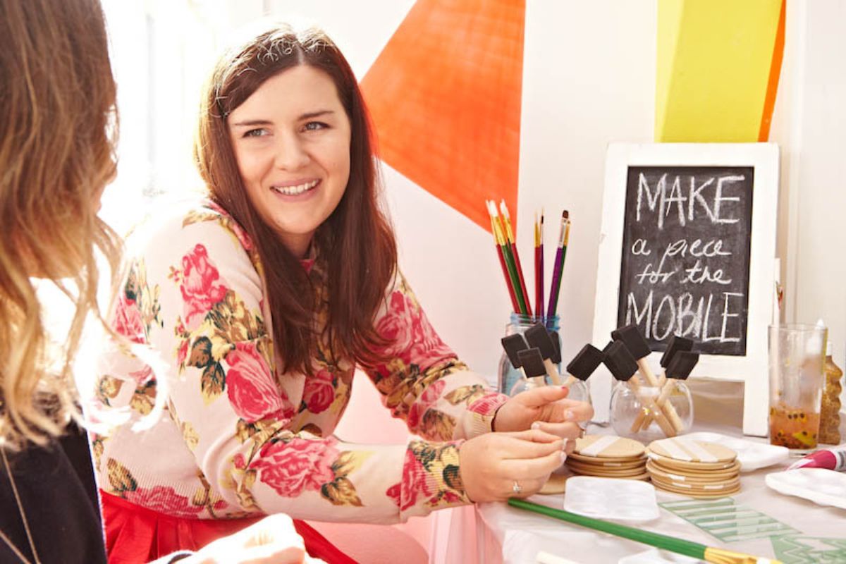 A woman in a floral dress sitting amongst craft supplies.