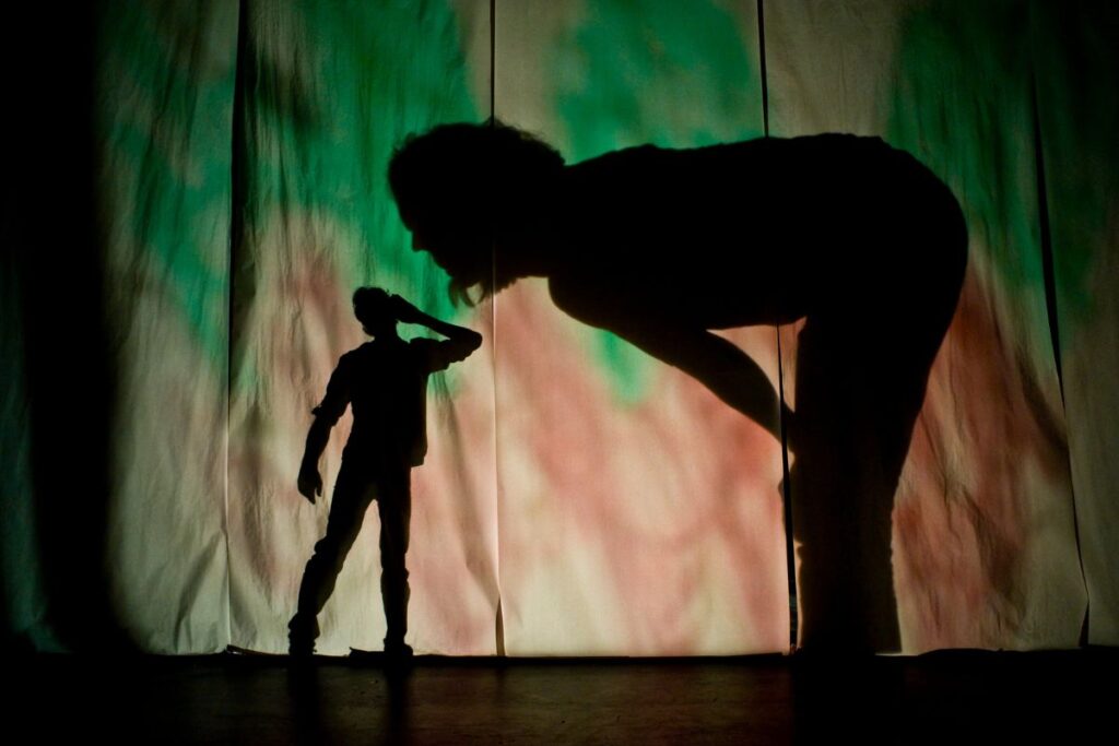Me & My Shadow childrens production a man extending an ear to a giant woman bending down to hear - shadows projected against a colourful sheets.