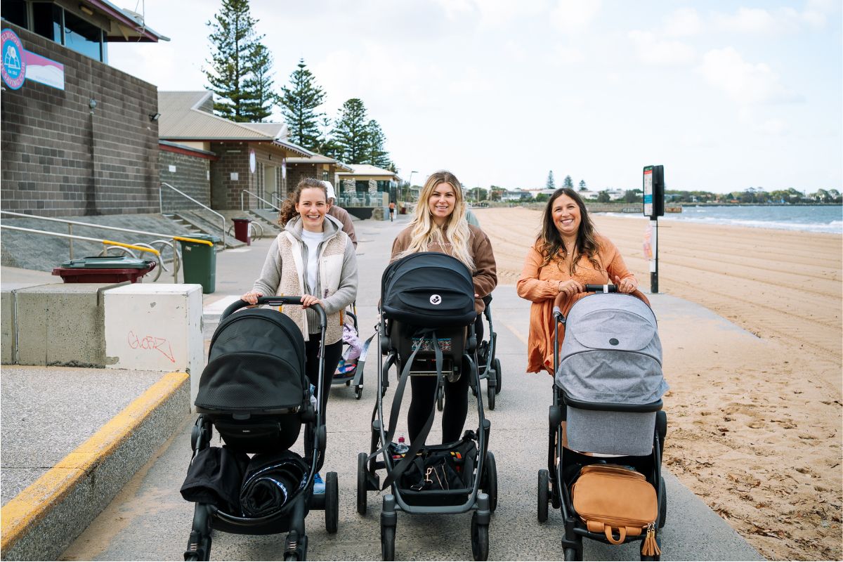 3 mums with strollers walking together along a beach pathway.