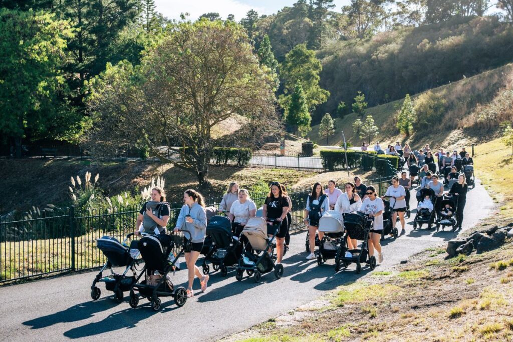 A group of people walking along a path, pushing strollers and enjoying a sunny day outdoors.
