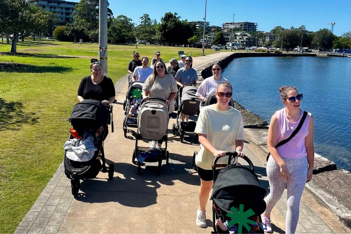 A group of mums with strollers on a walk alongside a river.