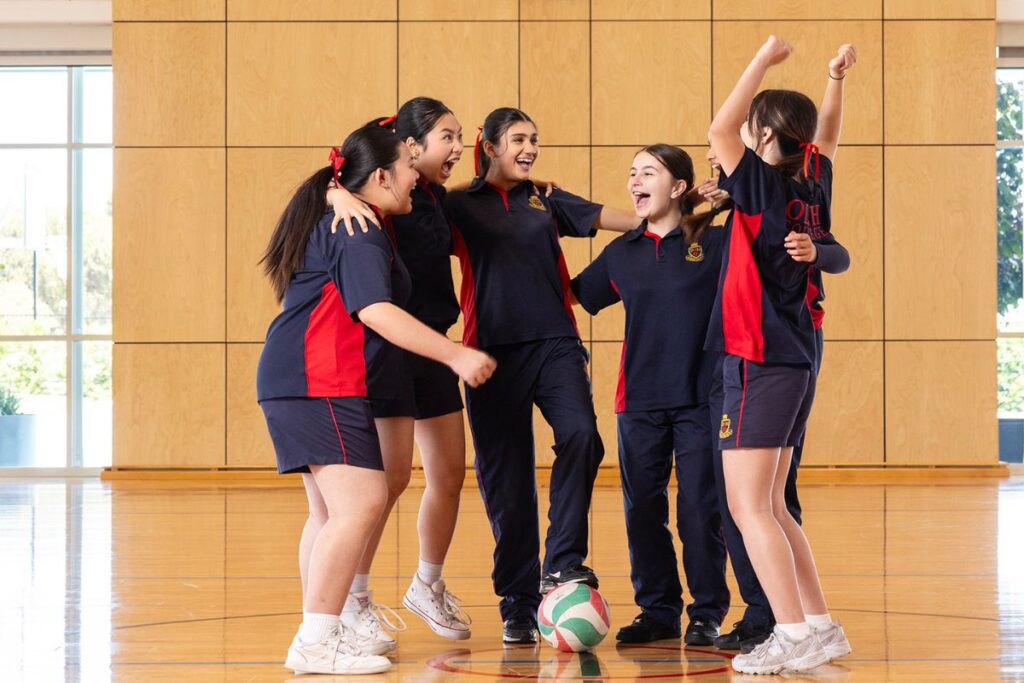 A group of school girls in sports uniform on a in indoor basketball court.