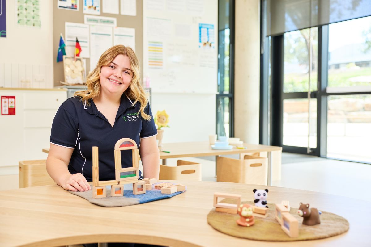 A teacher sitting at a classroom table with play equipment.