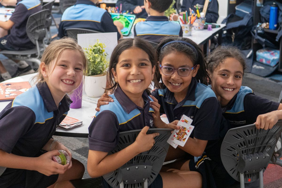 A group of Good Shepherd school students in school uniform sit together playing cards.