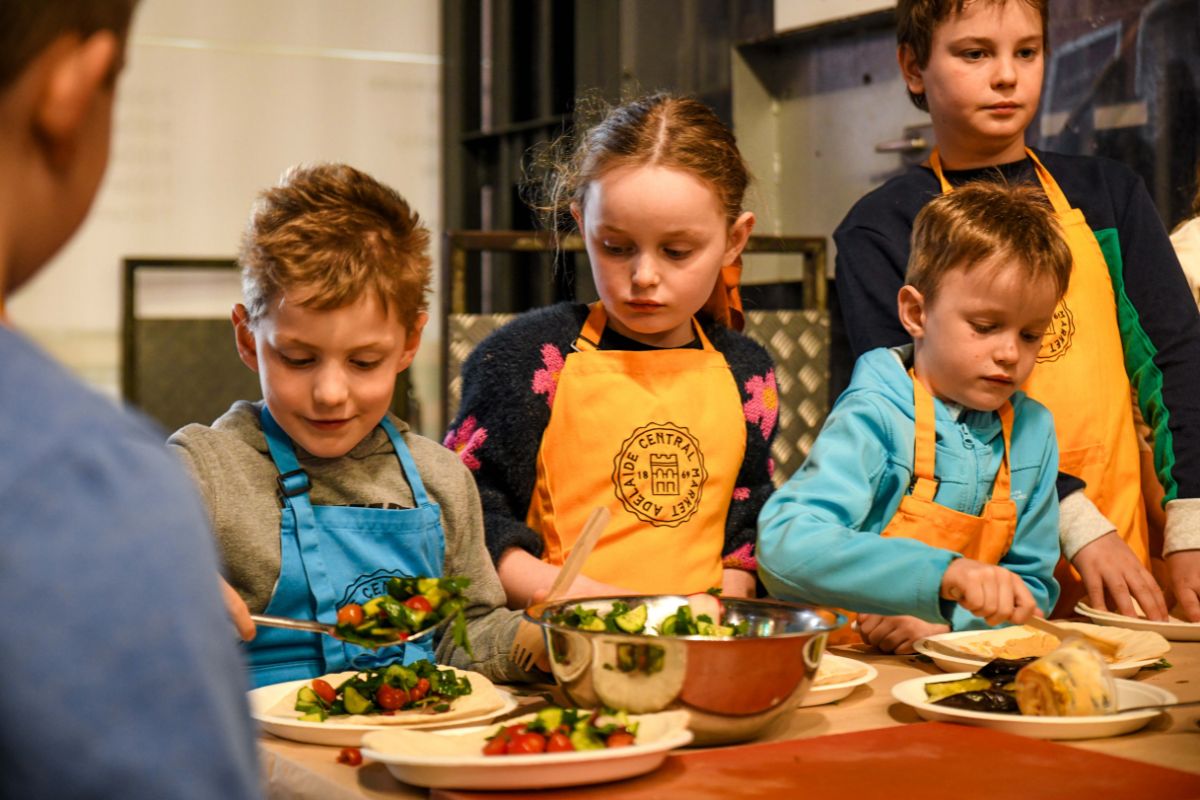 Children in Adelaide Central Market aprons preparing fresh ingredients during a Little Market Chefs cooking class at Adelaide Central Market