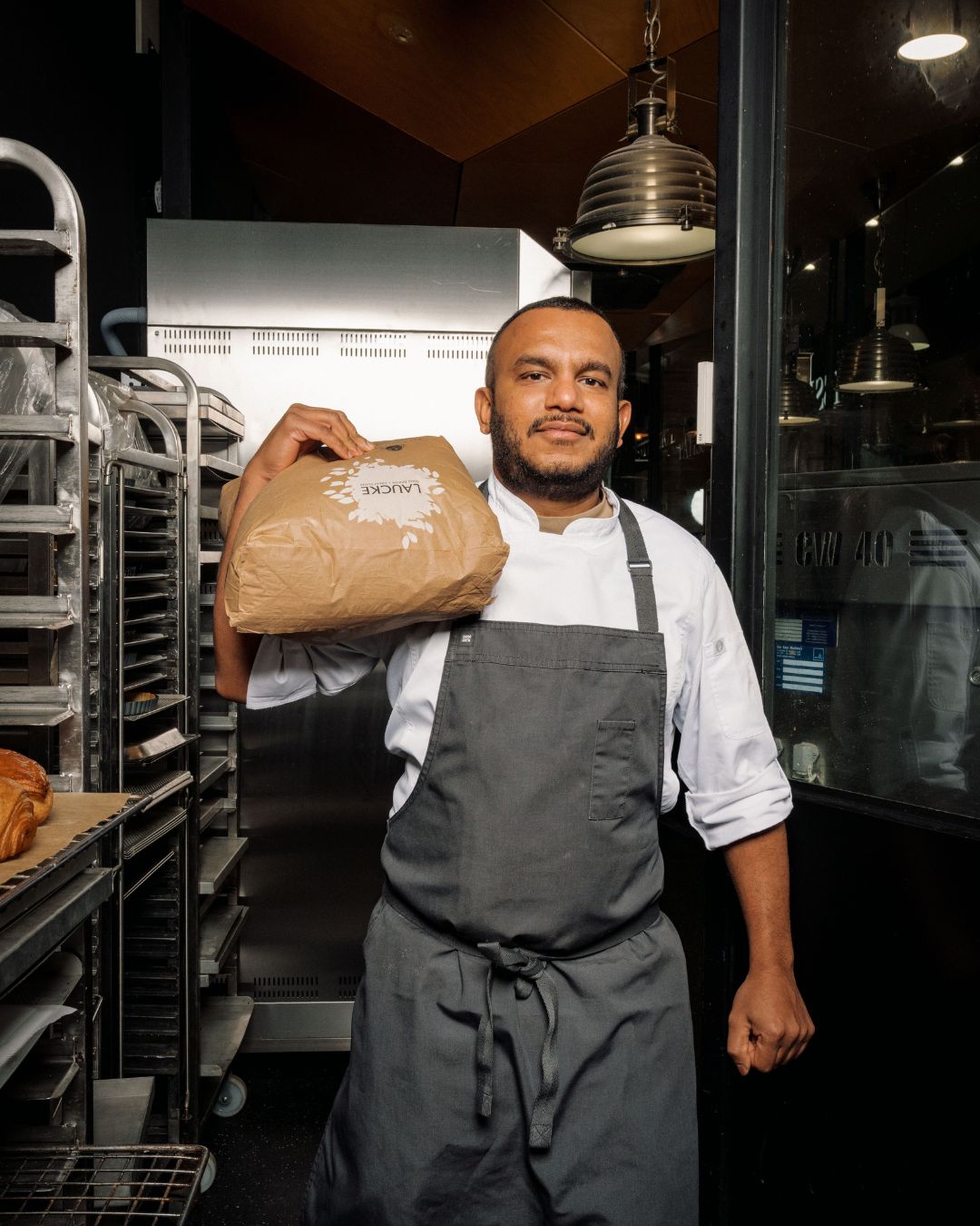An Adelaide's Finest baker in whites and apron holds a bag of flour in the bakery kitchen