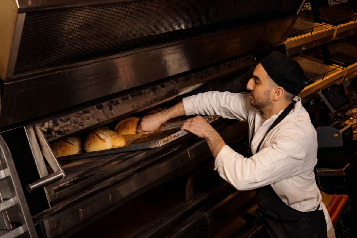 An Adelaide's Finest baker pulls freshly baked sourdough loaves from the oven