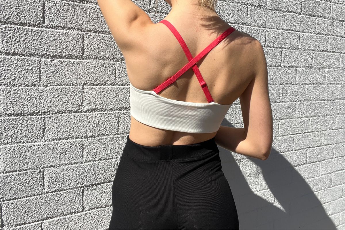 Back view of a model wearing a Billie Green white crop top with interchangeable red straps and black ribbed shorts.