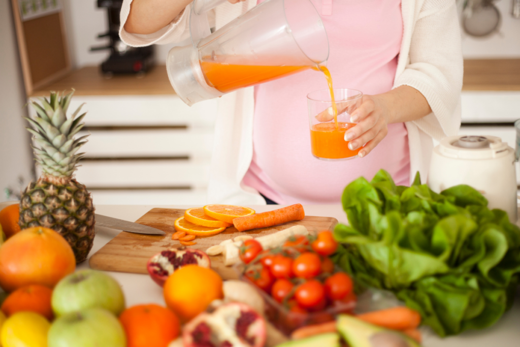 A pregnant woman is preparing a healthy meal and pouring a carrot juice.