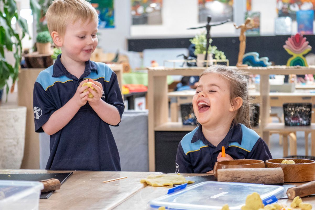 Two Good Shepherd Lutheran School ELC children laughing together while playing with playdough in the Curiosity ELC classroom.