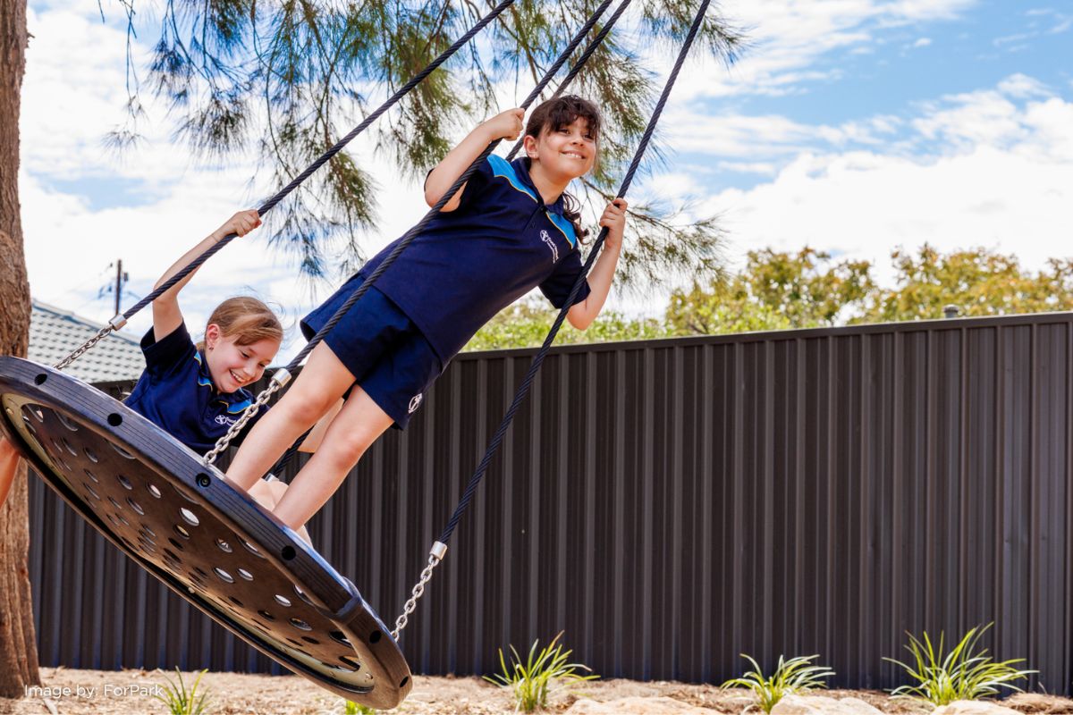 Two Good Shepherd Lutheran School students smiling while playing on a disc swing in the school playground