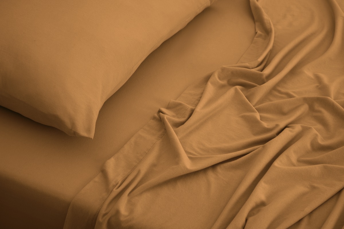 Close-up of It-Fits jersey cotton sheets and pillowcase in warm ginger, showing the soft, draped texture of the knitted fabric.