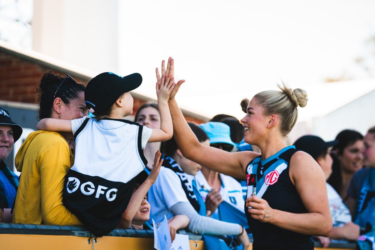 Port Adelaide AFLW player high-fiving a young fan over the fence at Alberton Oval after a Power home game
