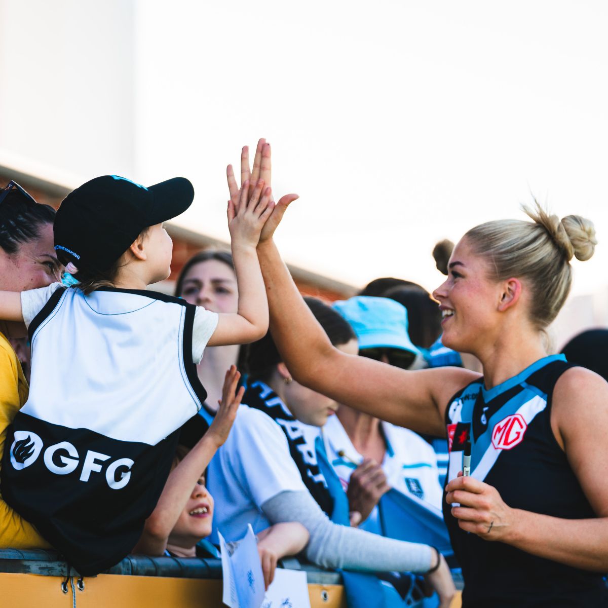 Port Adelaide AFLW player high-fiving a young fan over the fence at Alberton Oval after a Power home game