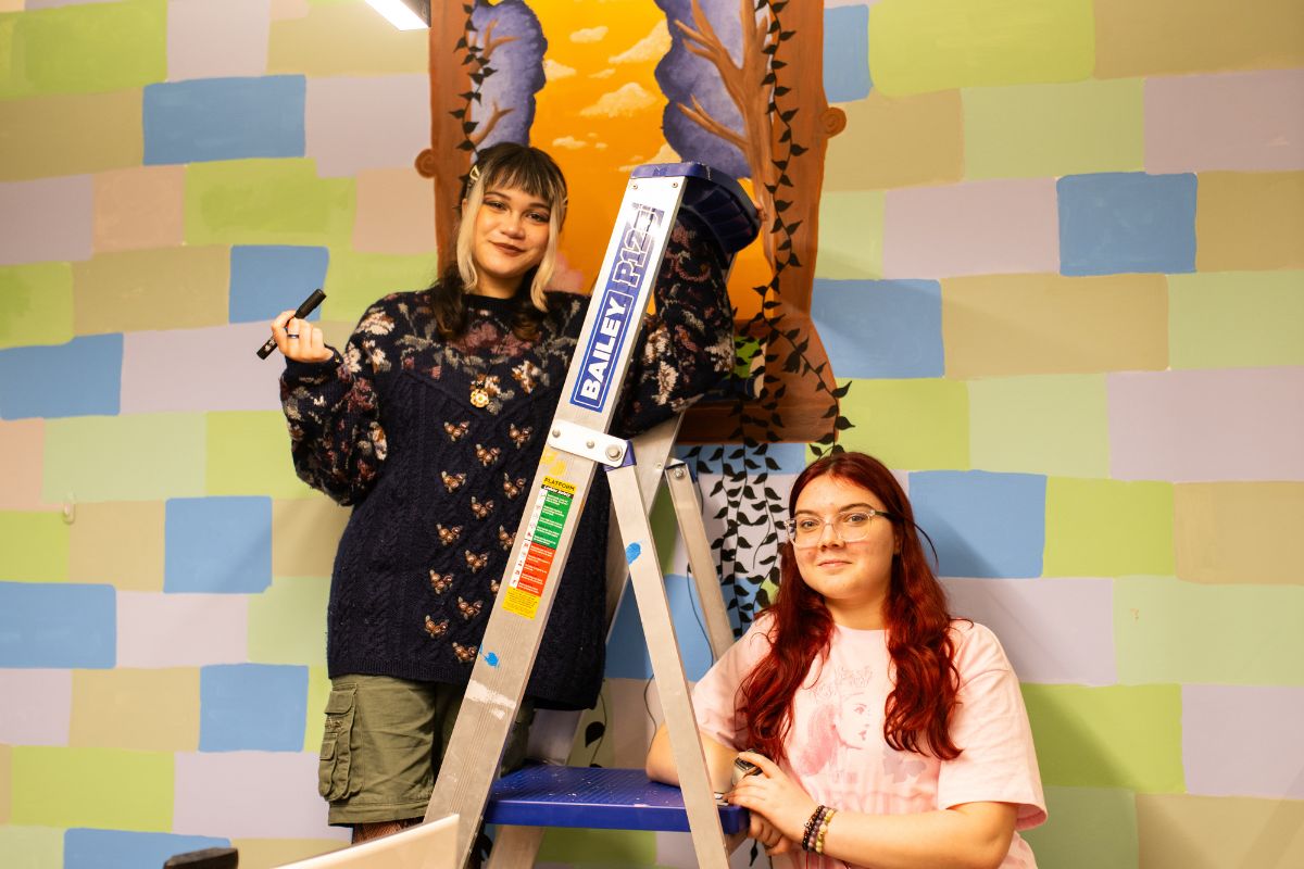 Two SASY students painting a mural together using a ladder and paint roller