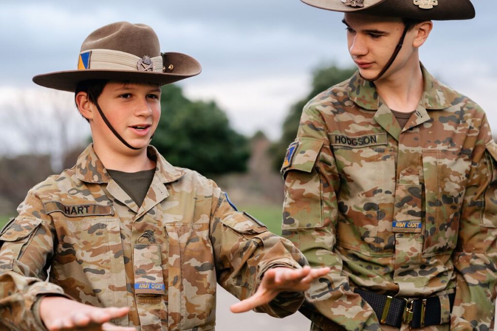 Two Tatachilla Army Cadets in uniform and broad-brimmed hats chat outdoors on campus.