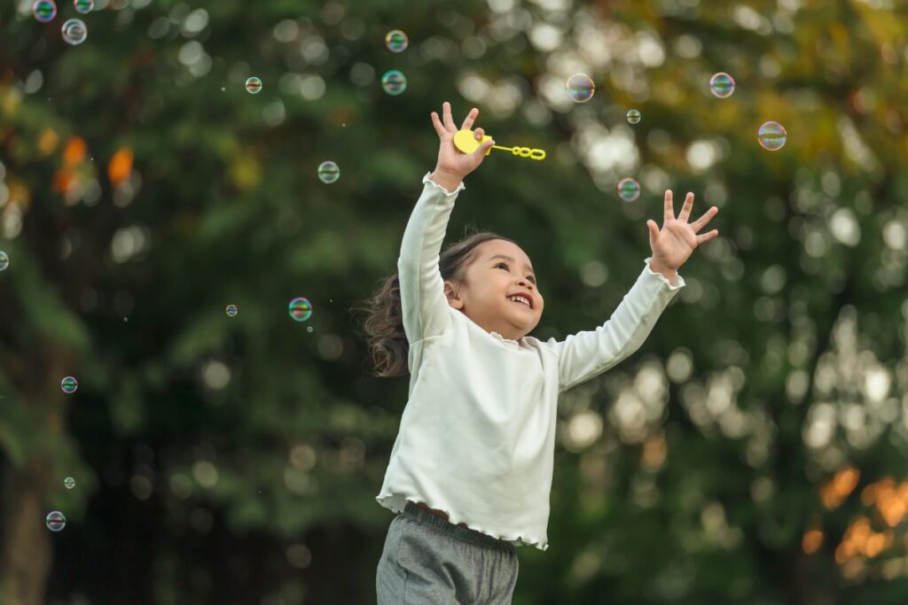 Tatachilla-Wonder_begins_here_1200x800.jpg A young child plays outdoors with a bubble wand, arms raised joyfully amid floating bubbles.
