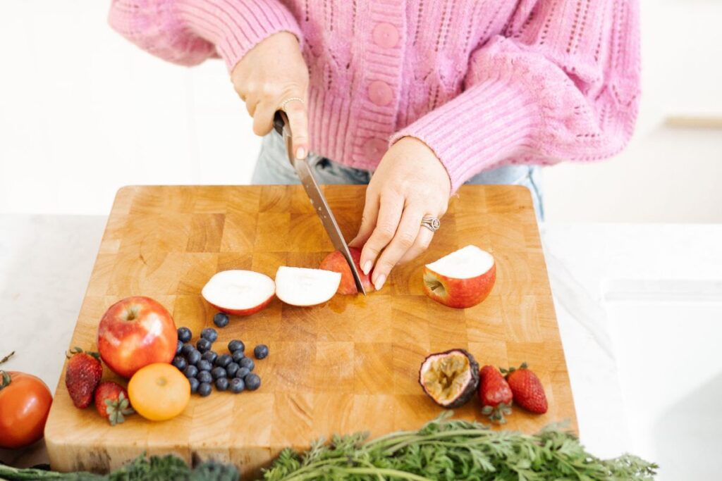 A woman wearing a pink jumper chopping an apple on a wooden chopping board.