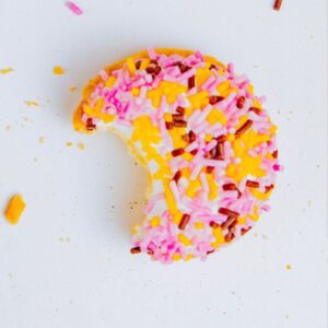 Round biscuit decorated with pink and yellow icing and sprinkles, half iced and half plain