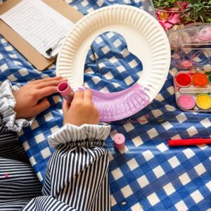Child's hands decorating a paper plate wreath with pressed flowers and leaves under contact paper
