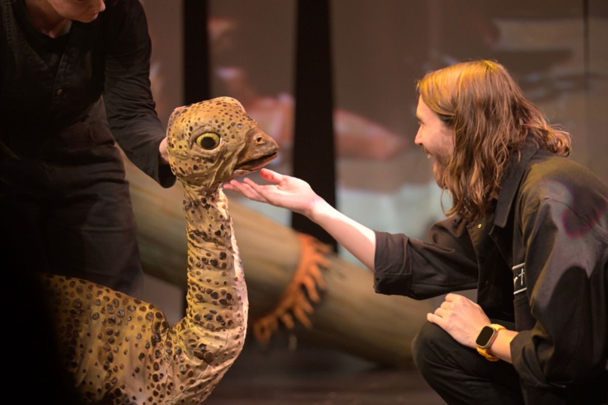 A performer gently interacts with a small dinosaur puppet in Erth's Dinosaurs