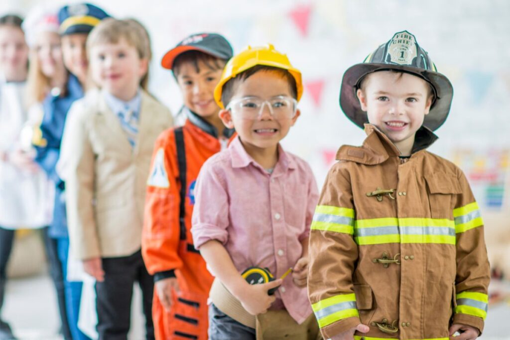 Kids dressed in career costumes, including a firefighter and a construction worker, lined up together indoors