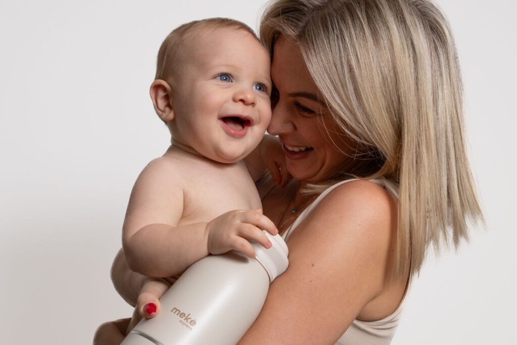 Mum holding smiling baby, cream Meke Express bottle.