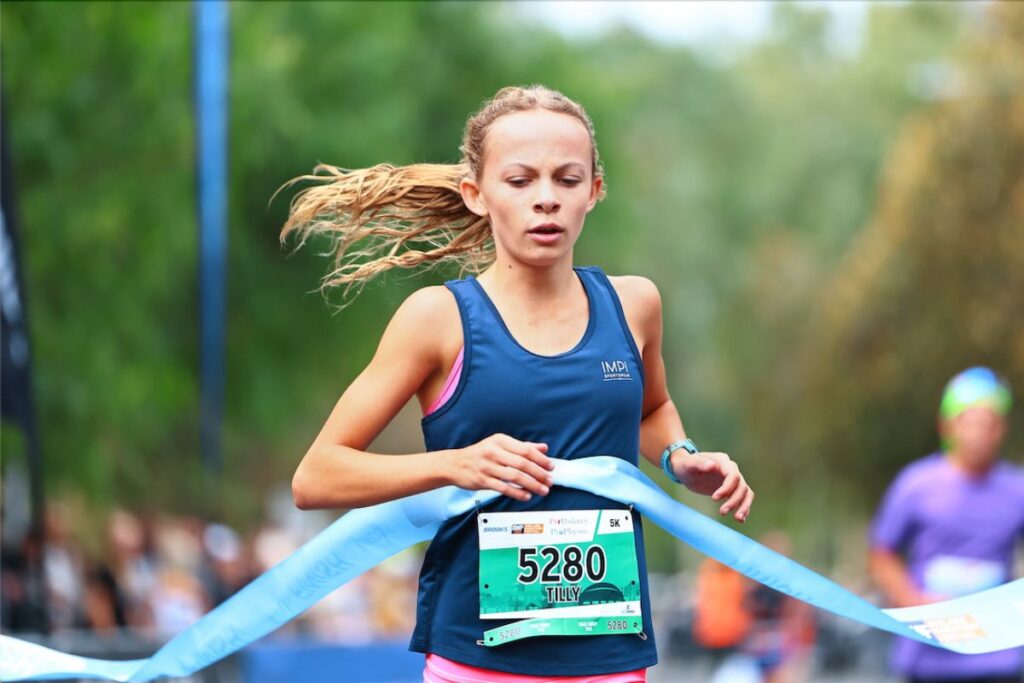A young anthlete crossing the finish line tape at the Adelaide Marathon Festival.