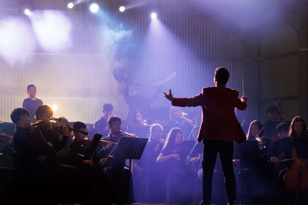 A conductor leads Adelaide Youth Orchestras inside a Stratco big shed with dramatic stage lighting